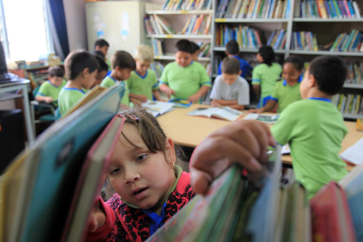 In a library in northern Aruba, a girl selects a book while her classmates read (Photo: UNICEF/Roger LeMoyne).