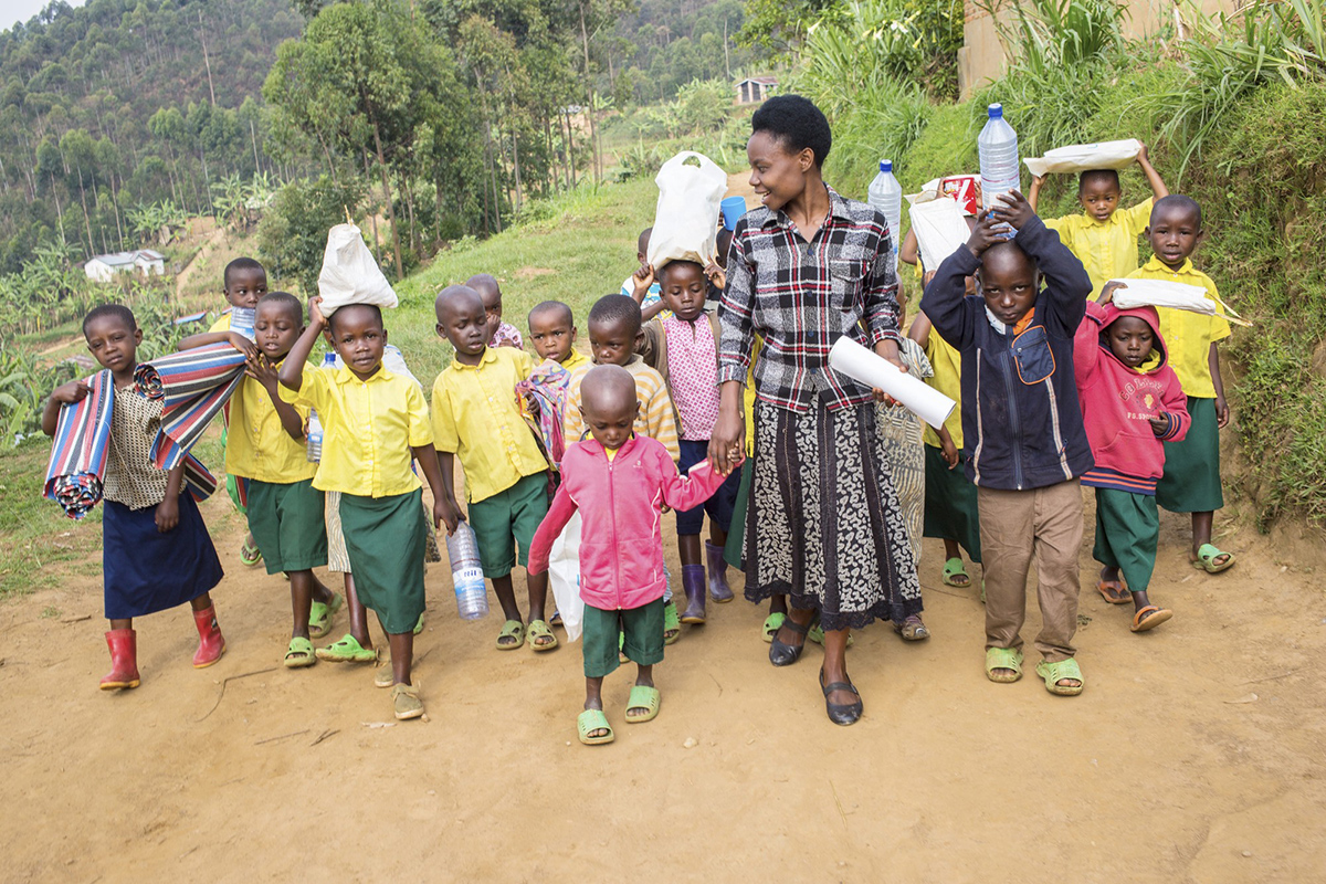 Teacher Josephine Nyirampuhwe, 28, walks to school in the morning assisted by some of her young pupils. Â©VSO/Alice Kayibanda
