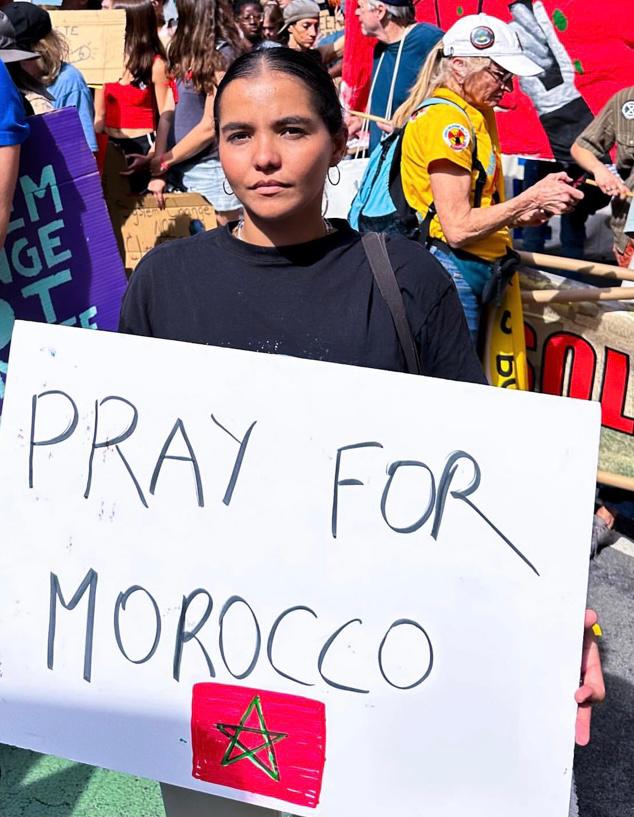 Yasmina holding a sign that says 'Pray for Morocco'.